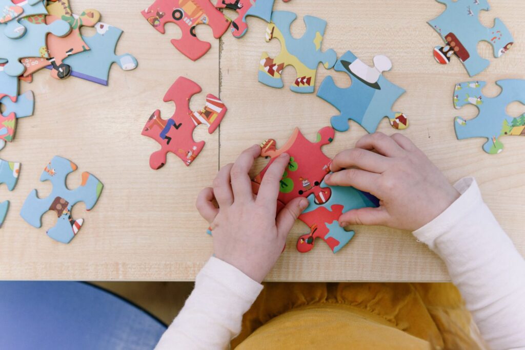 Close-up of child assembling colorful puzzle pieces on a wooden table, top view.