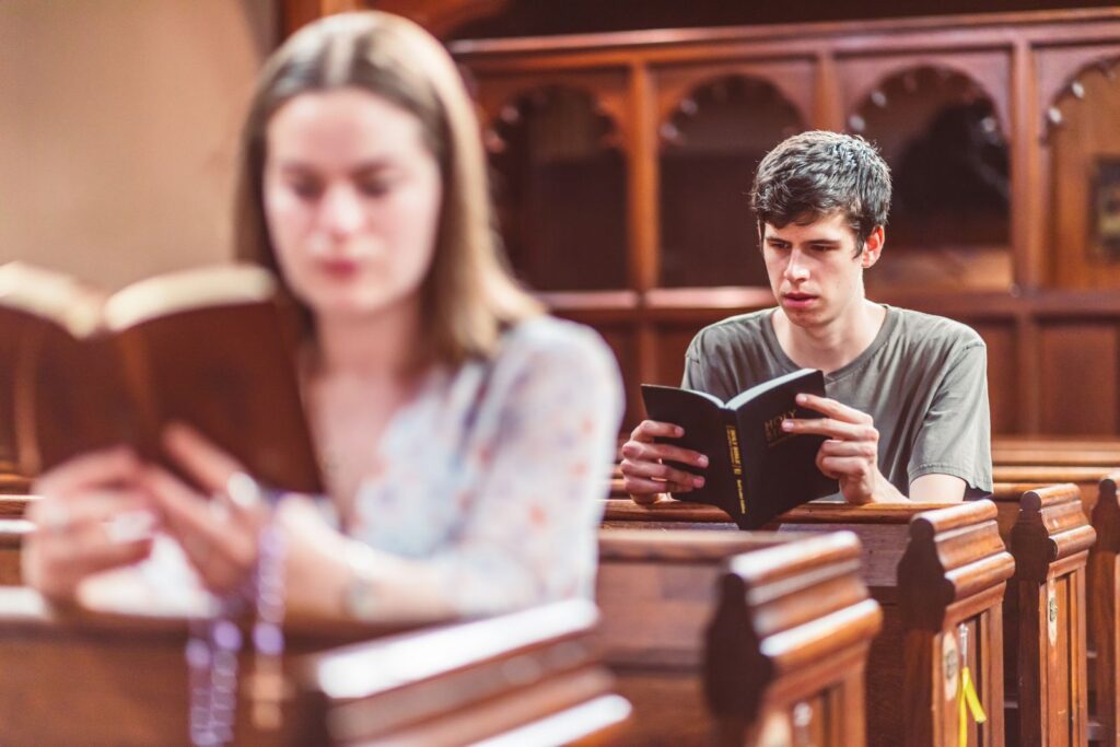 A man reading a book inside a church, with a woman blurred in the foreground.
