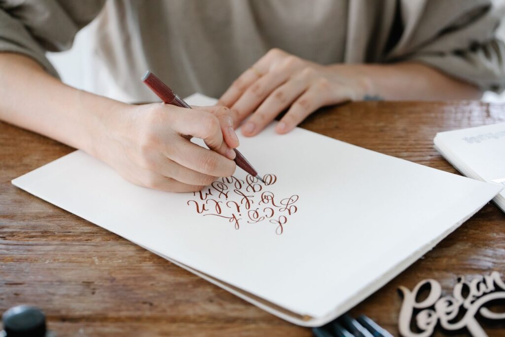 A person practicing calligraphy on paper with a pen, showcasing beautiful lettering.
