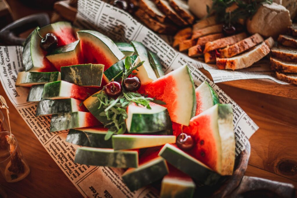 Sliced watermelon with cherries and bread on a rustic serving platter.