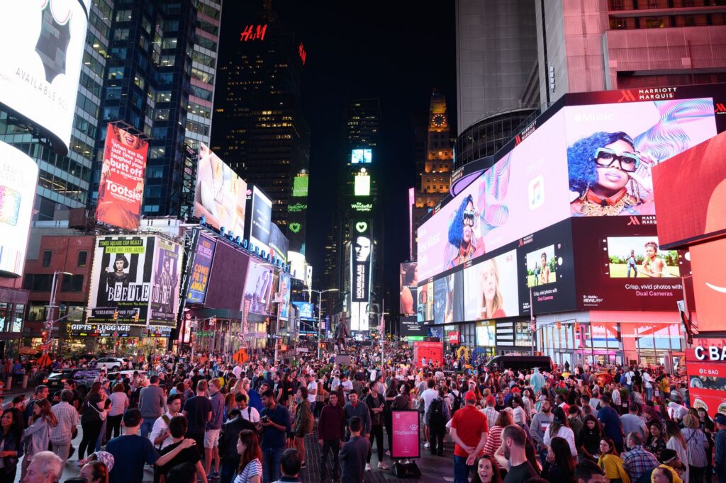 Crowds gather under the neon lights of iconic Times Square in New York City at night.