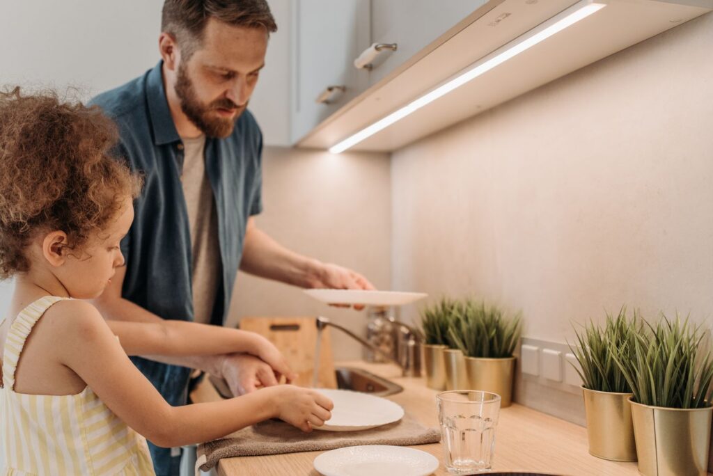 A father and daughter bonding while washing dishes in a modern kitchen.