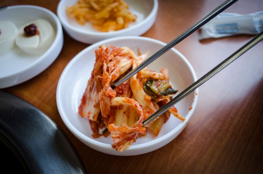 Close-up of traditional Korean kimchi in a ceramic bowl with chopsticks on a wooden surface.