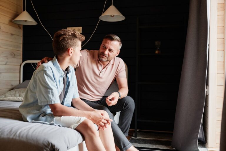 A father bonding with his teenage son in a cozy bedroom, sharing advice and conversation.