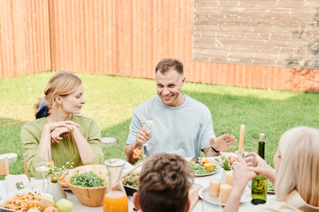 A family enjoying a cheerful meal together outdoors in a sunny backyard setting.