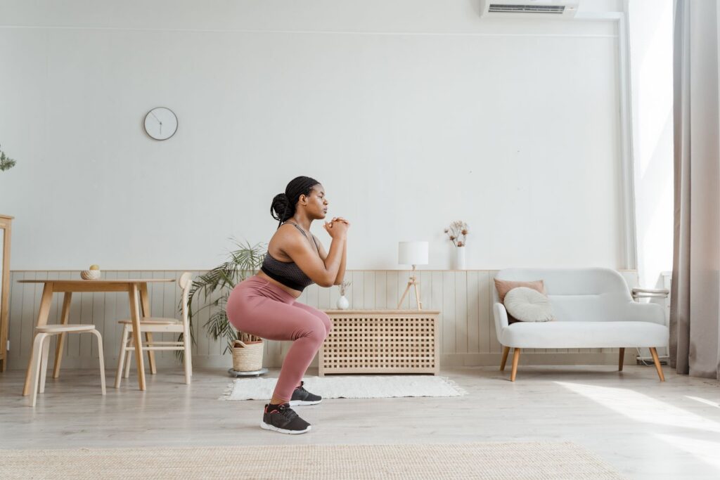 Woman in activewear doing squats at home, promoting a healthy lifestyle and fitness routine.