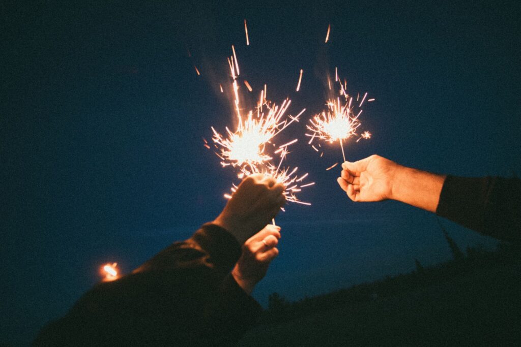 Hands holding sparklers illuminate the night, creating a festive atmosphere during an outdoor celebration.