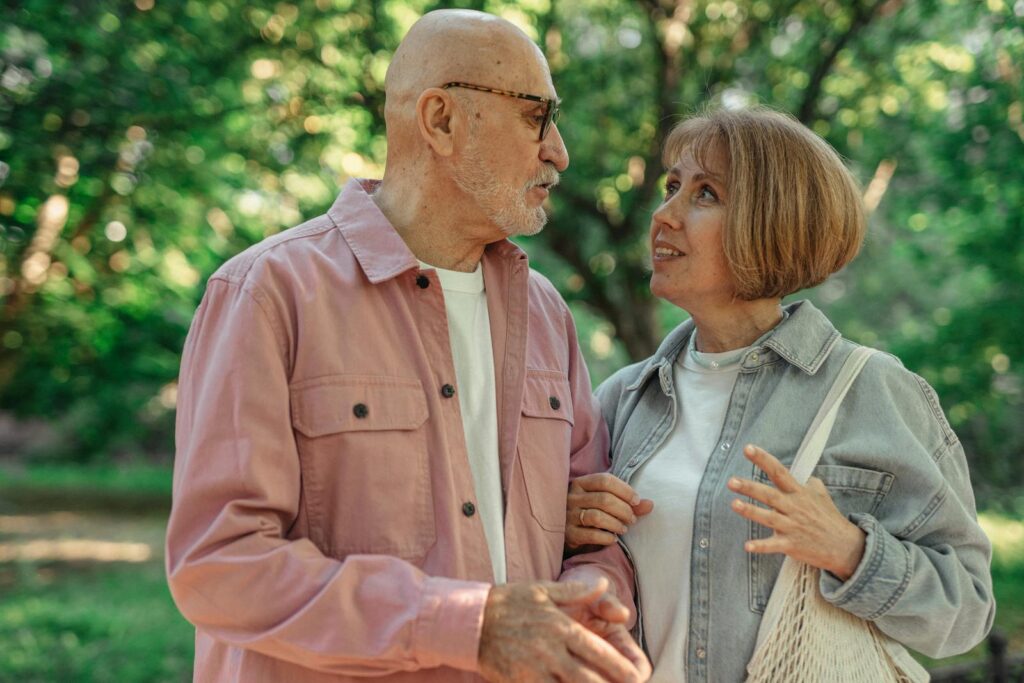 An elderly couple shares a joyful conversation in a vibrant green park setting.