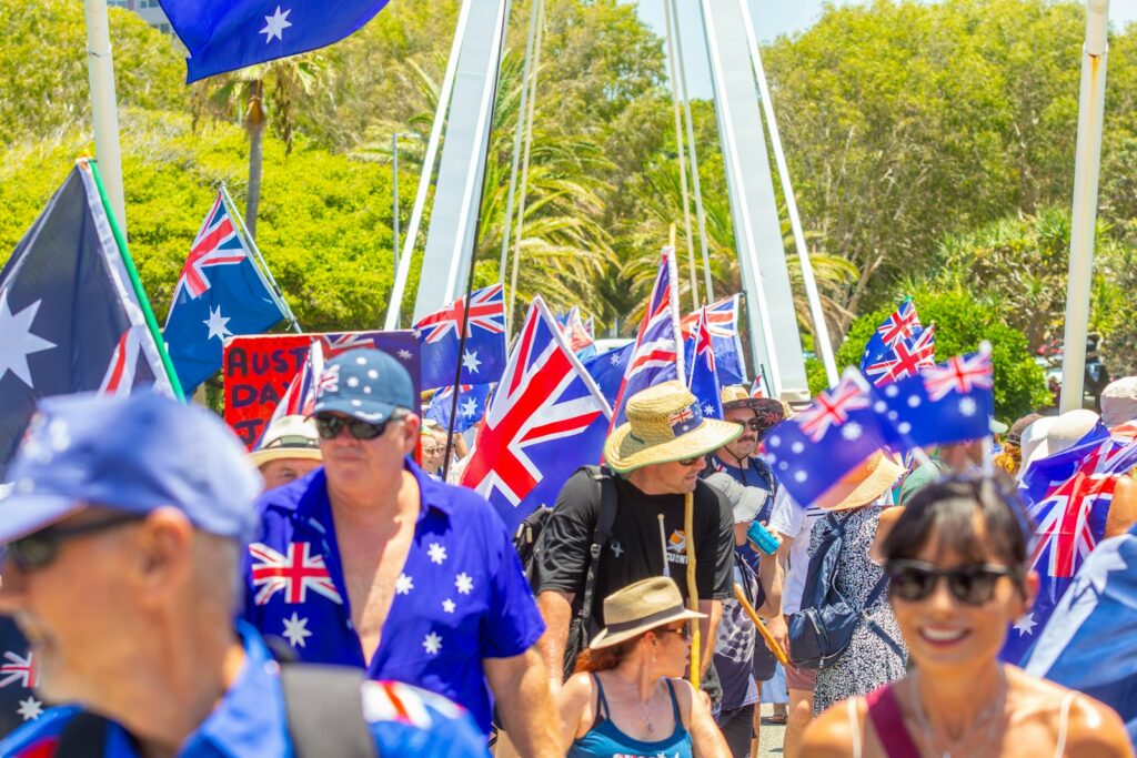 Crowd of people waving australian flags during a sunny day.