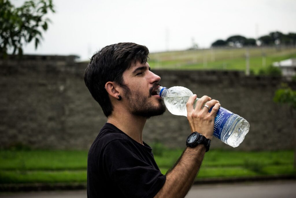 A young man drinks bottled water outside, staying hydrated and refreshed.