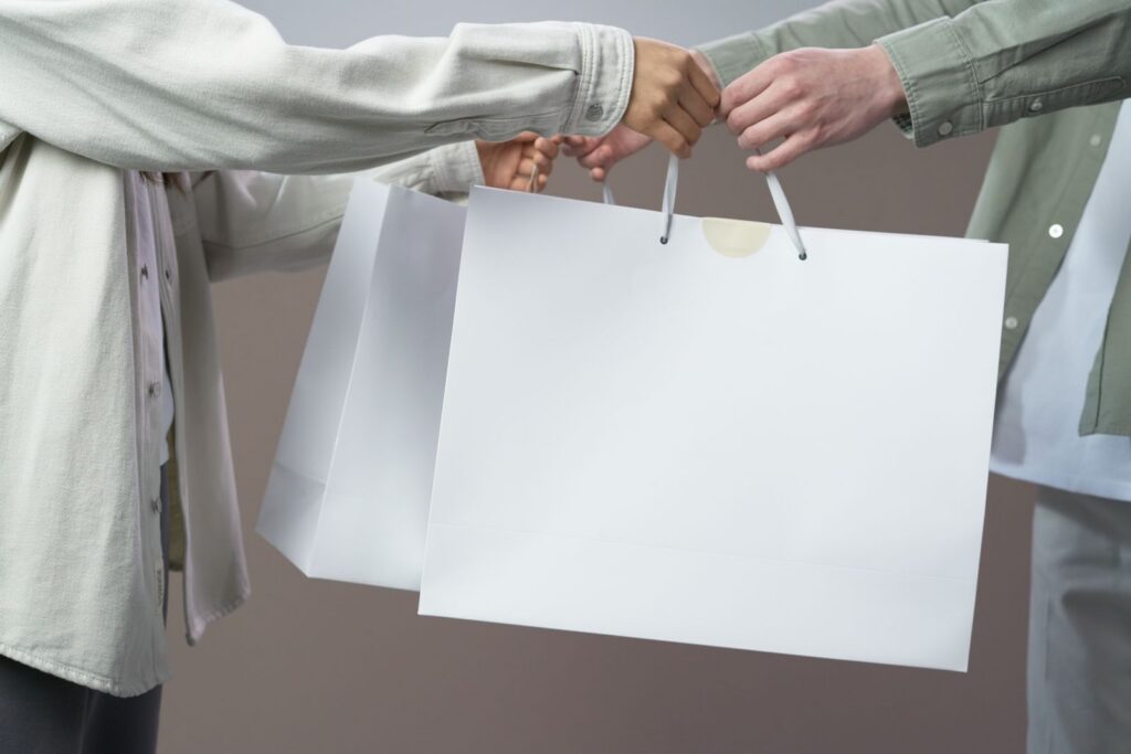 Midsection view of two people exchanging white shopping bags indoors.