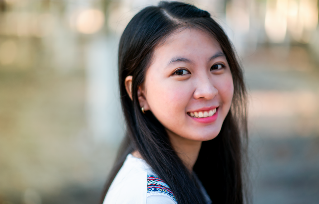 A joyful young woman smiling warmly outdoors. Close-up portrait with a soft background blur.