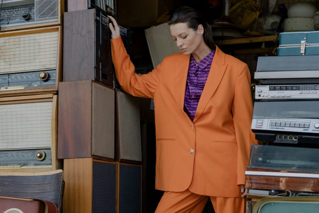Stylish woman in orange outfit posing among vintage cassette players and speakers.