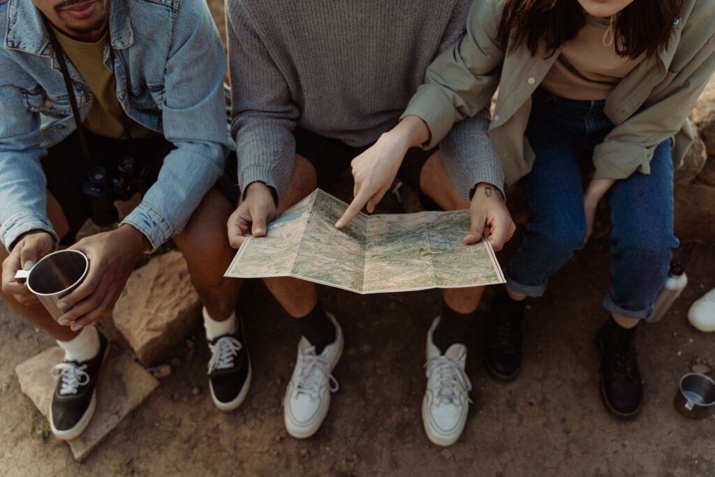 Group of friends sitting together, exploring a map for their next adventure, creating exciting travel plans.