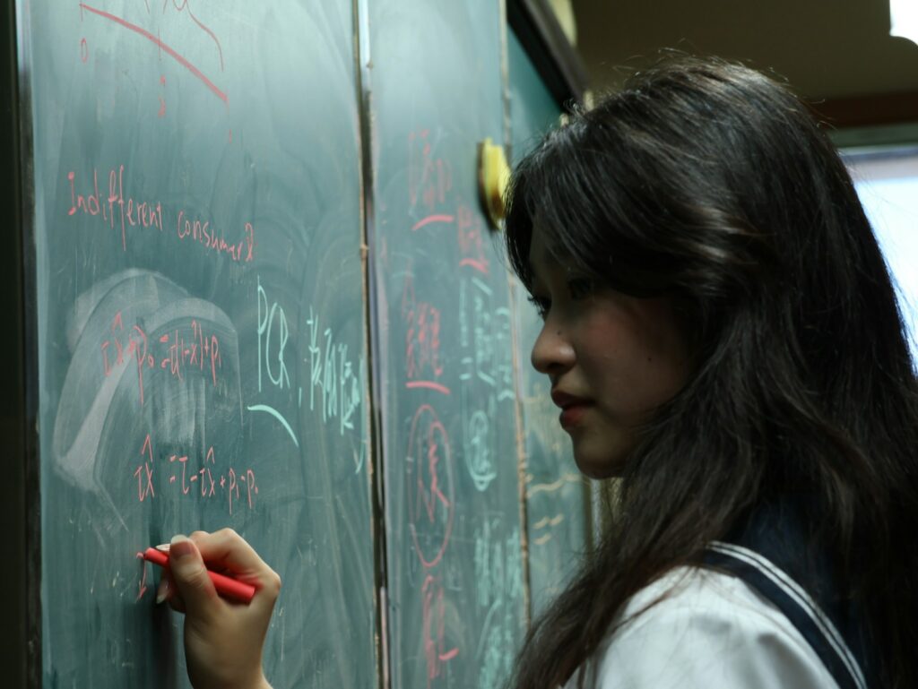 A student writes on a blackboard in a classroom.