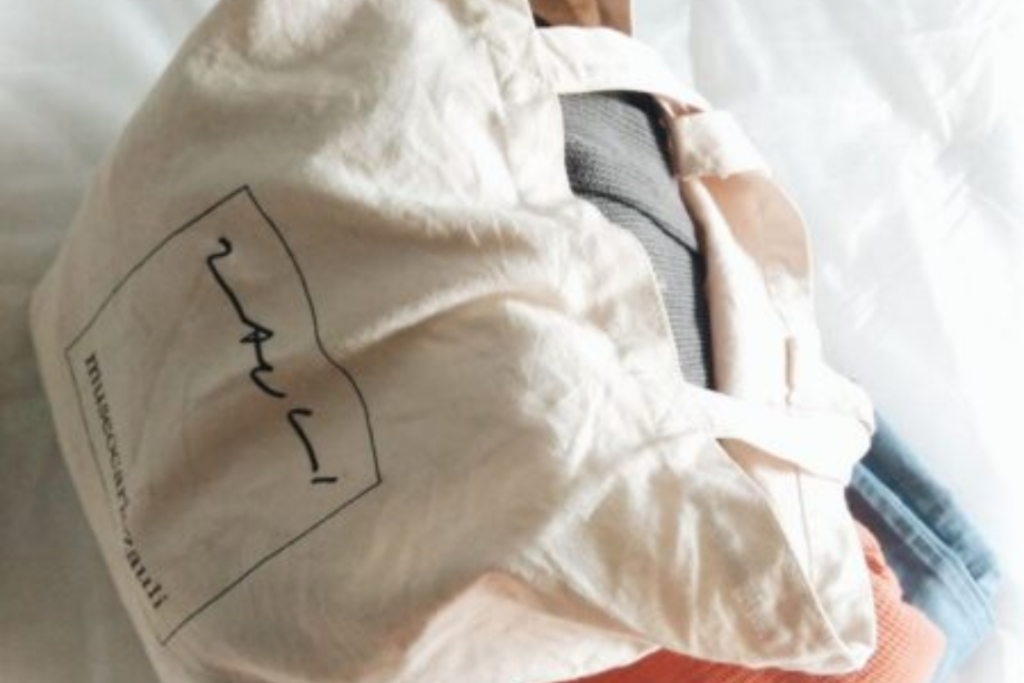A natural cotton tote bag filled with clothes for donation