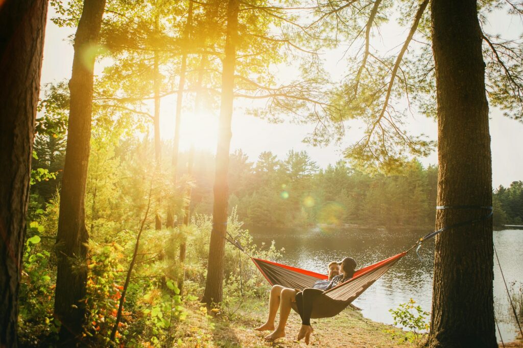 man and woman seating on gray hammock beside trees during daytime