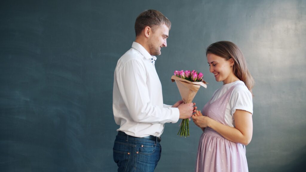 Man gives woman flowers in front of dark background.