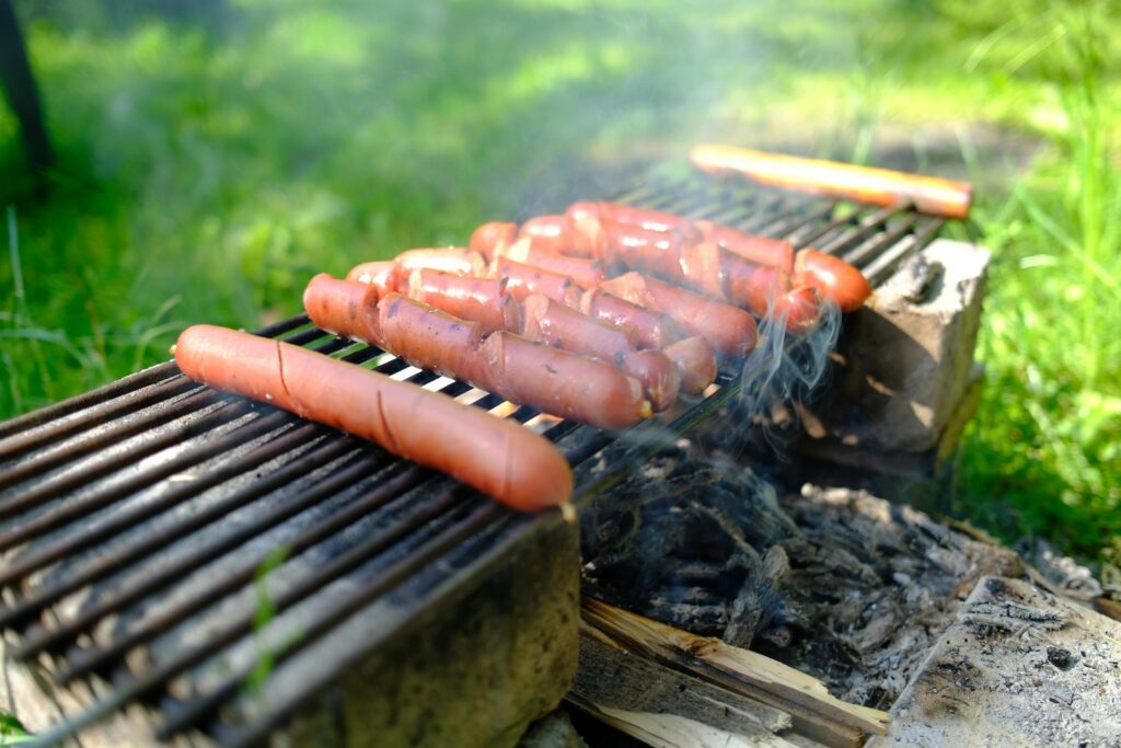 Hot dogs cooking on a grill over an open fire.