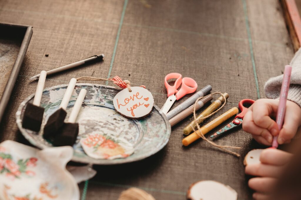 Child writing on a tag amidst craft supplies.