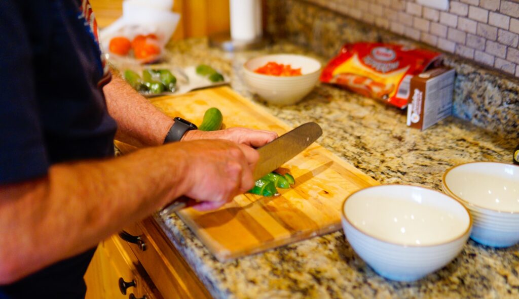 A person chopping green vegetables on a wooden cutting board.