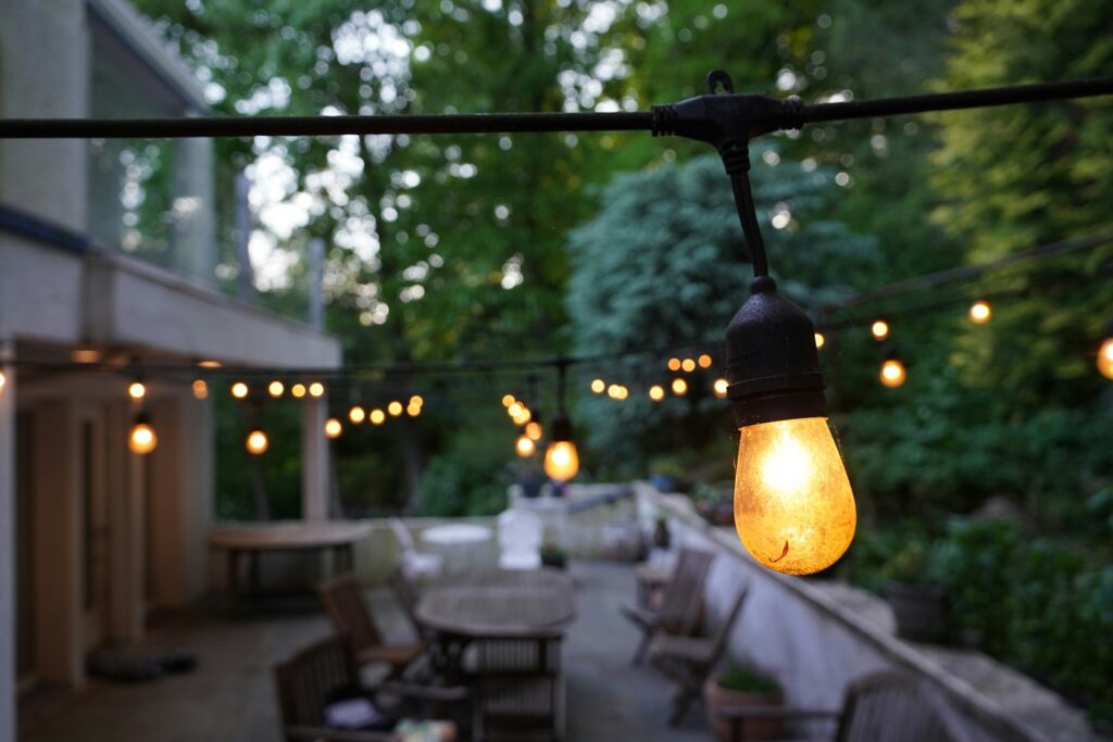 String lights illuminate an outdoor patio with tables and chairs.