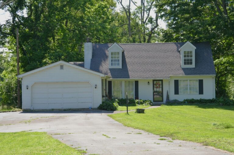 A white house with a garage, driveway, and green lawn.