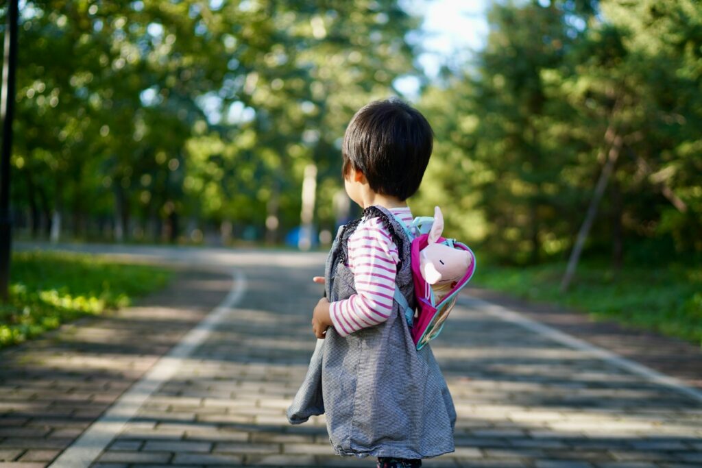 A young child with a backpack walks on a path.
