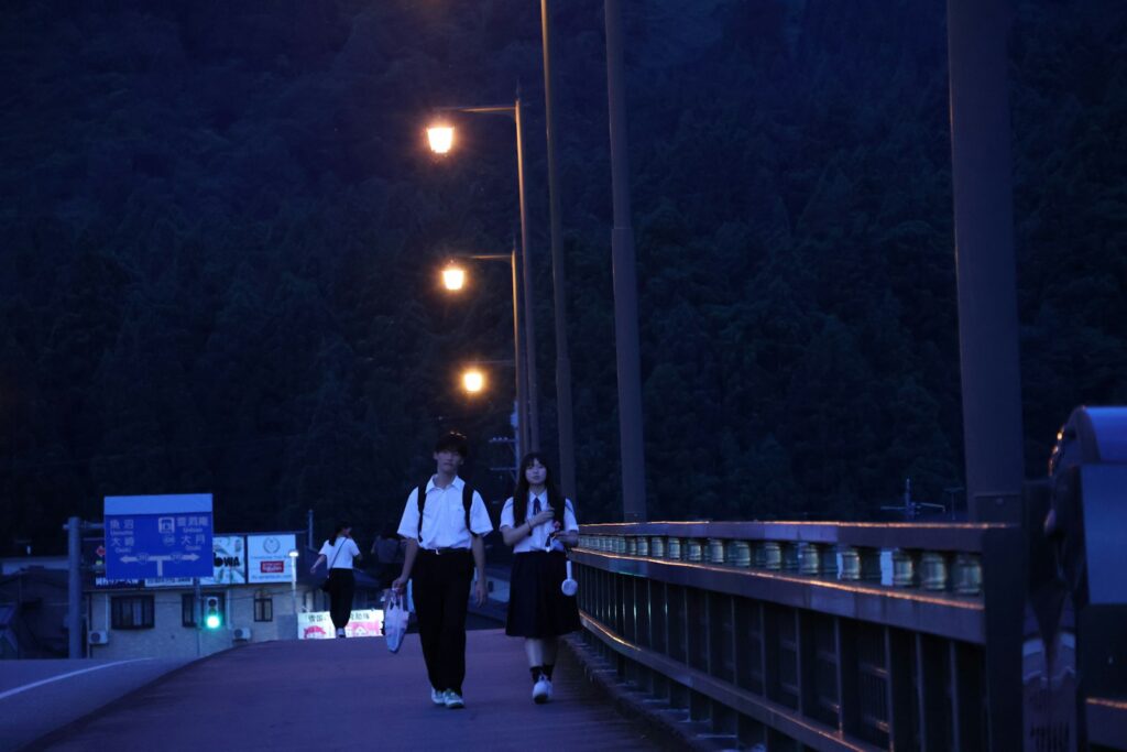 A couple of people walking across a bridge at night
