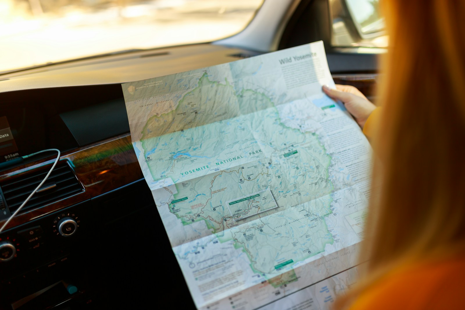 passenger unfolding a large paper road map in a car