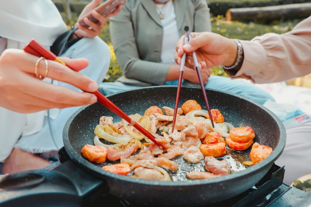 two people cooking food in a pan on a stove