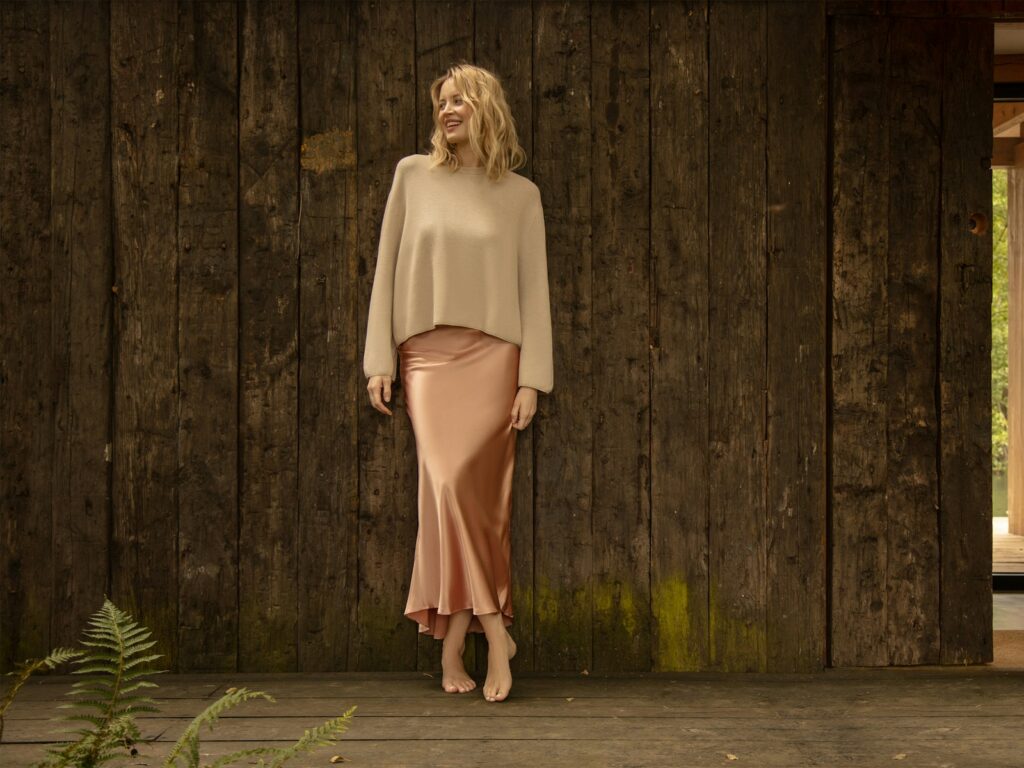 A woman poses elegantly against wood.