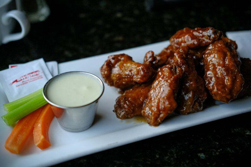 Glazed chicken wings with dipping sauce, celery, and carrots.