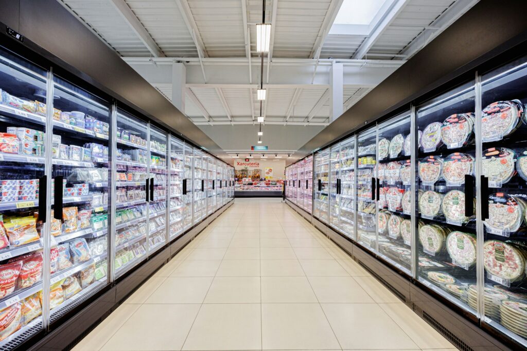 A long aisle in a brightly lit supermarket with refrigerators.