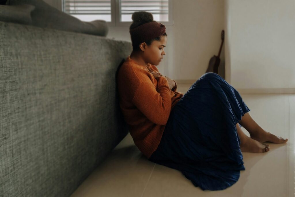 Woman in orange sitting on the floor and looking vulnerablle