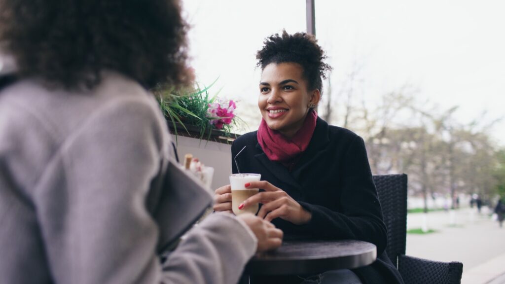 Two women talking at a cafe with coffee.