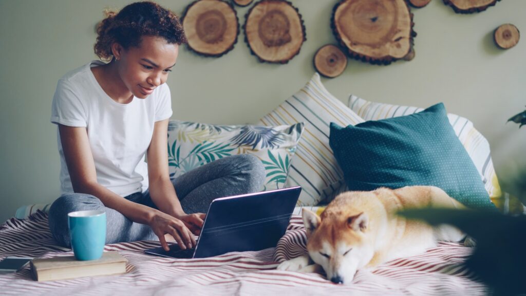 Woman works on laptop with dog in a cozy space.