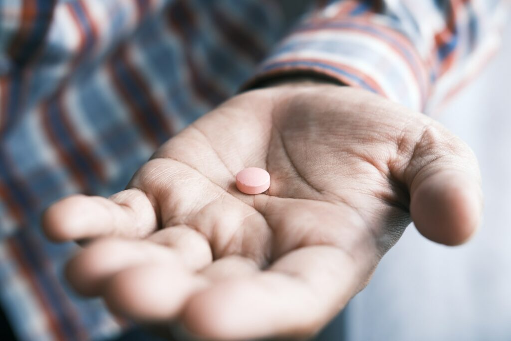 person holding pink round supplement pill