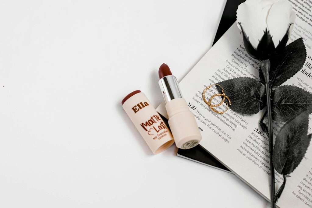 Red lipstick, white rose, and rings on an open book.