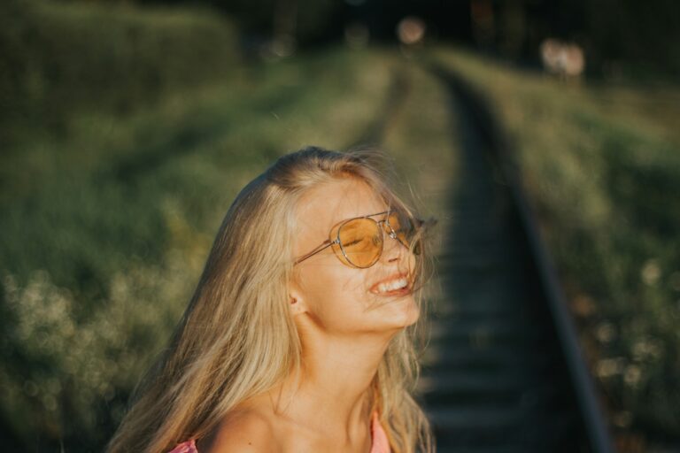 A young woman with blonde hair wearing sunglasses smiles.