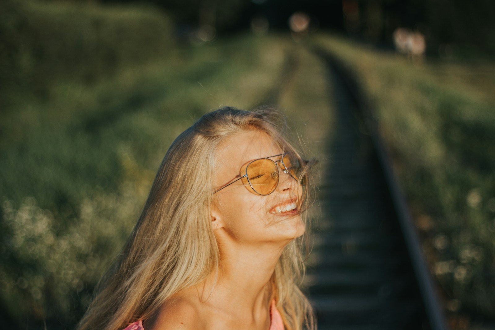 A young woman with blonde hair wearing sunglasses smiles.
