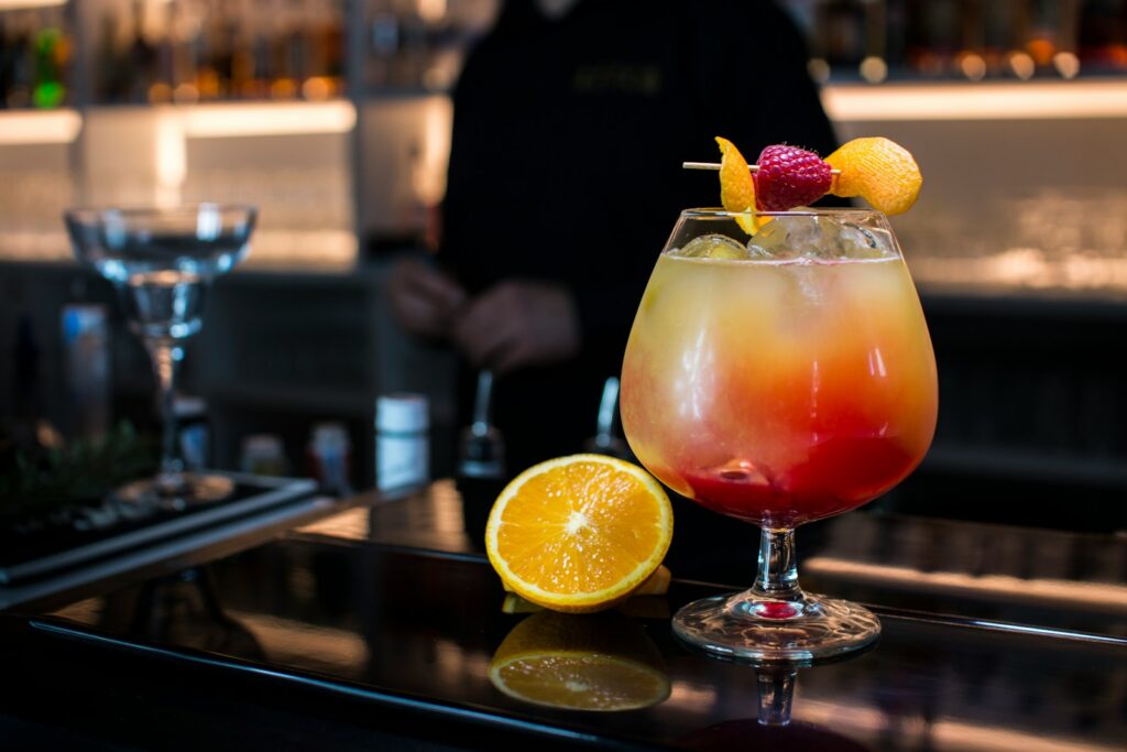 A colorful layered cocktail with fruit garnish and orange slice.
