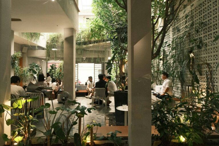 People dining in a lush, modern cafe with plants.