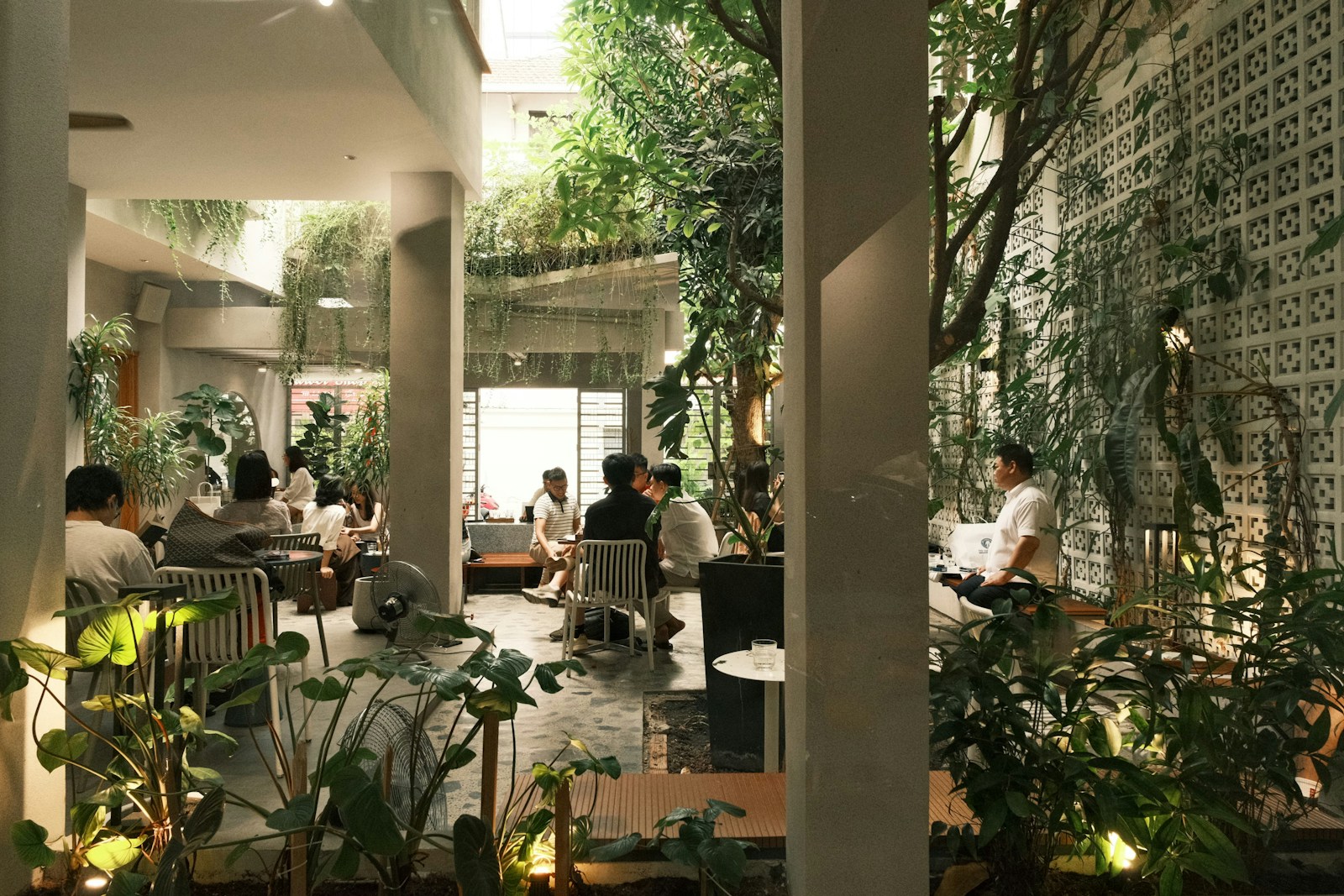 People dining in a lush, modern cafe with plants.