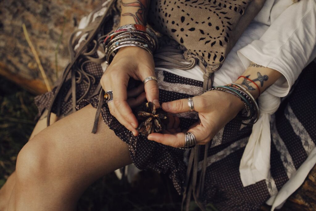 Close-up of hands with jewelry holding a pine cone in a bohemian style setting.