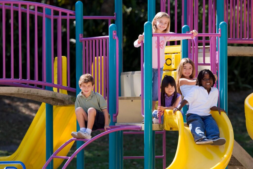A group of diverse children enjoying playground slides on a sunny day outdoors.