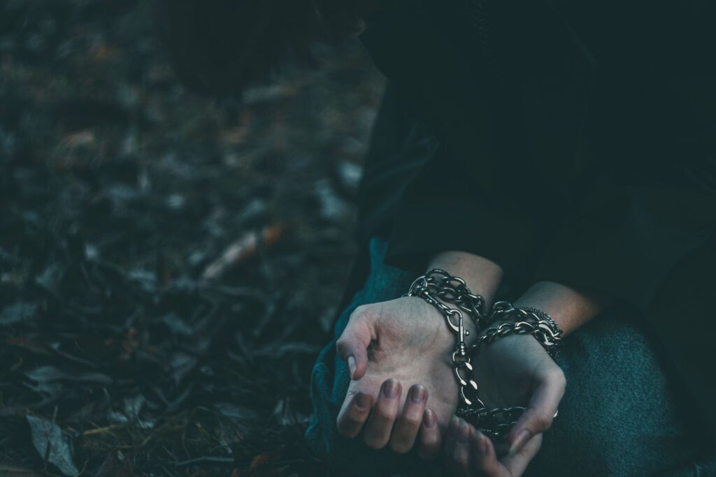 Close-up of a person's hands bound with chains in an outdoor setting, symbolizing confinement.