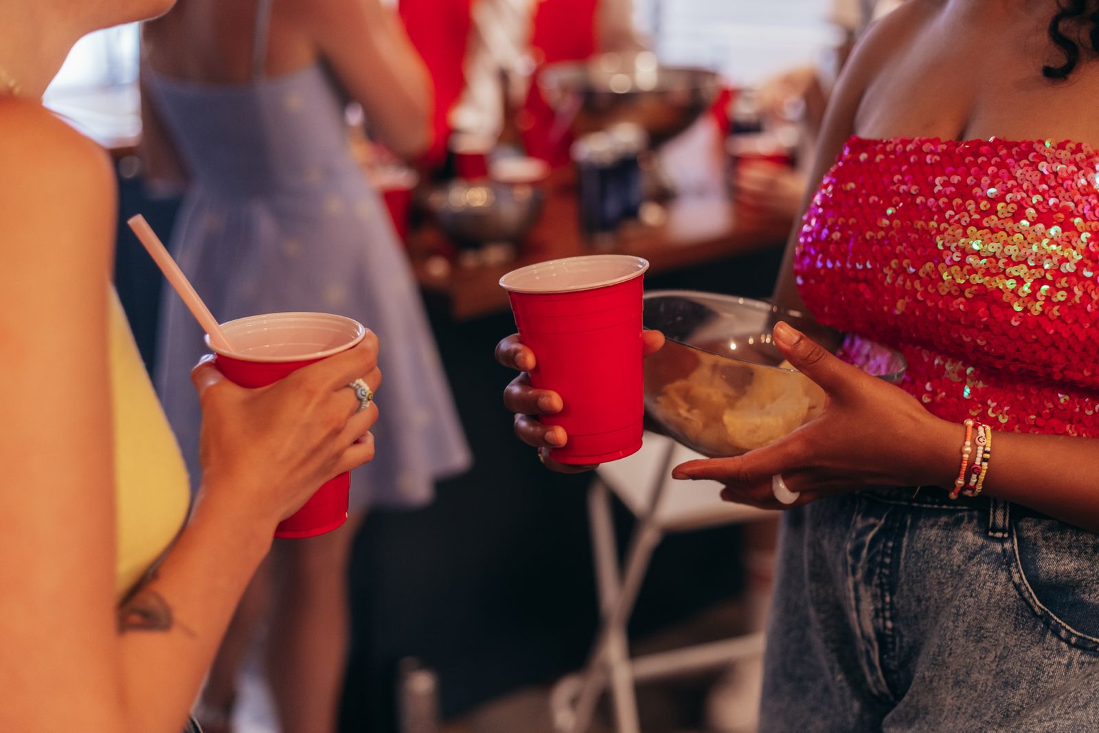Two women holding red party cups and snacks at a casual indoor gathering.