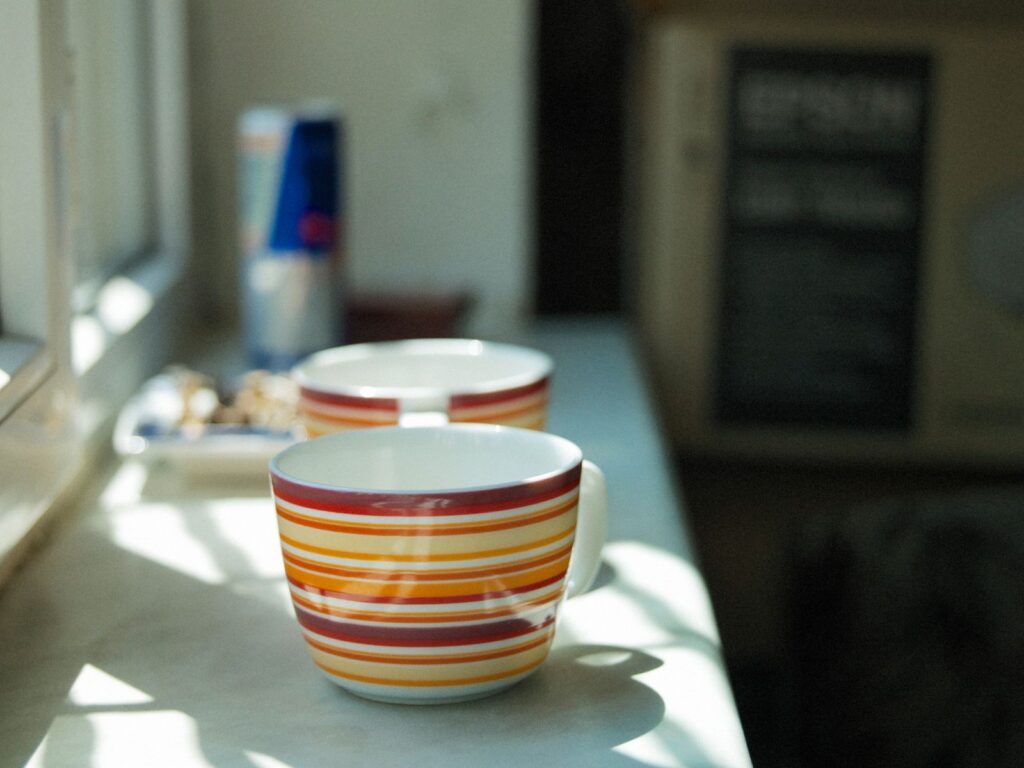 Vibrant ceramic cups with striped patterns on a sunlit kitchen counter.