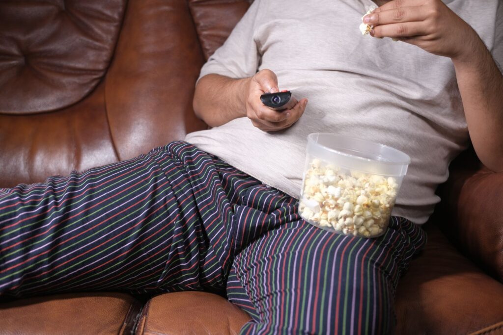 Person relaxing on a couch with popcorn and remote control, enjoying leisure time.